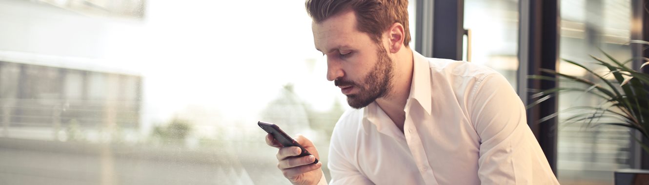 Man sitting by a window looking at his cell phone.